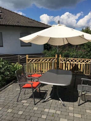 An outdoor patio with a table and chairs, an umbrella, and a wooden fence. - Miniappartement Zini (Lindlar)