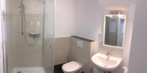 A bathroom with a glass-enclosed shower, a toilet, and a sink with a mirror above it. - Miniappartement Zini (Lindlar)