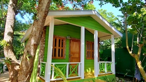 A small, green wooden house with a porch, surrounded by trees. - Bak A Yaad Overt Green Cottage (Negril)