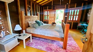 A wooden room with a bed, a nightstand, a lamp, and a decorative wall with star shapes. - Bak A Yaad Overt Green Cottage (Negril)