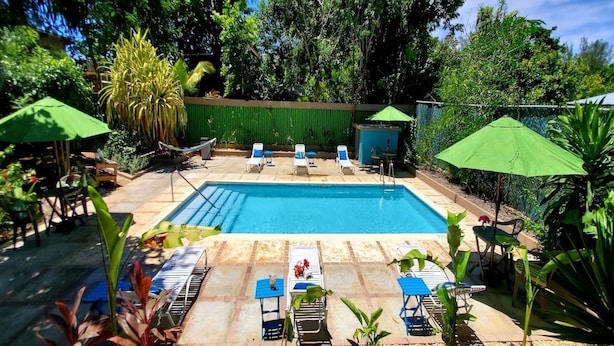 A rectangular swimming pool with lounge chairs and umbrellas. - Bak A Yaad Overt Green Cottage (Negril)
