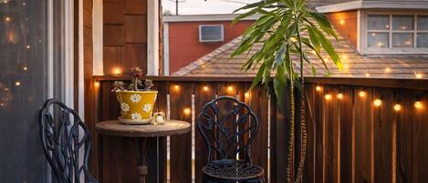 A wooden deck with string lights, two chairs, a small table, and a potted plant.