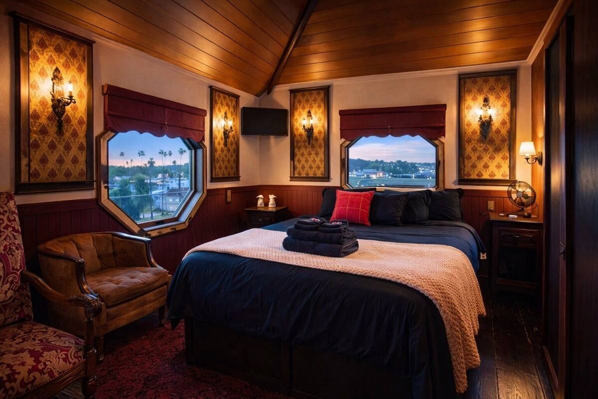 Une chambre d’hôtel avec un grand lit, deux tables de chevet, une chaise et une vue sur la ville grâce à de grandes fenêtres.