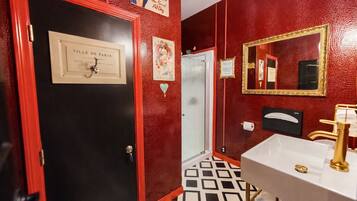 A bathroom with a red wall, a black door, a white sink with gold fixtures, and a mirror with a gold frame.
