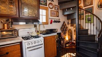 A kitchen with a stove, oven, and a small island. There is a staircase leading to a second floor.