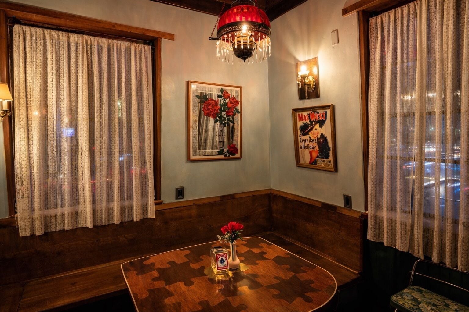 Una habitación acogedora con un banco de madera, una mesa con diseño de rompecabezas, un jarrón de flores rojas y un cartel de estilo vintage en la pared.
