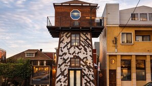 Un bâtiment doté d’une façade géométrique originale, une petite tour avec une fenêtre circulaire et un potelet d’incendie devant.