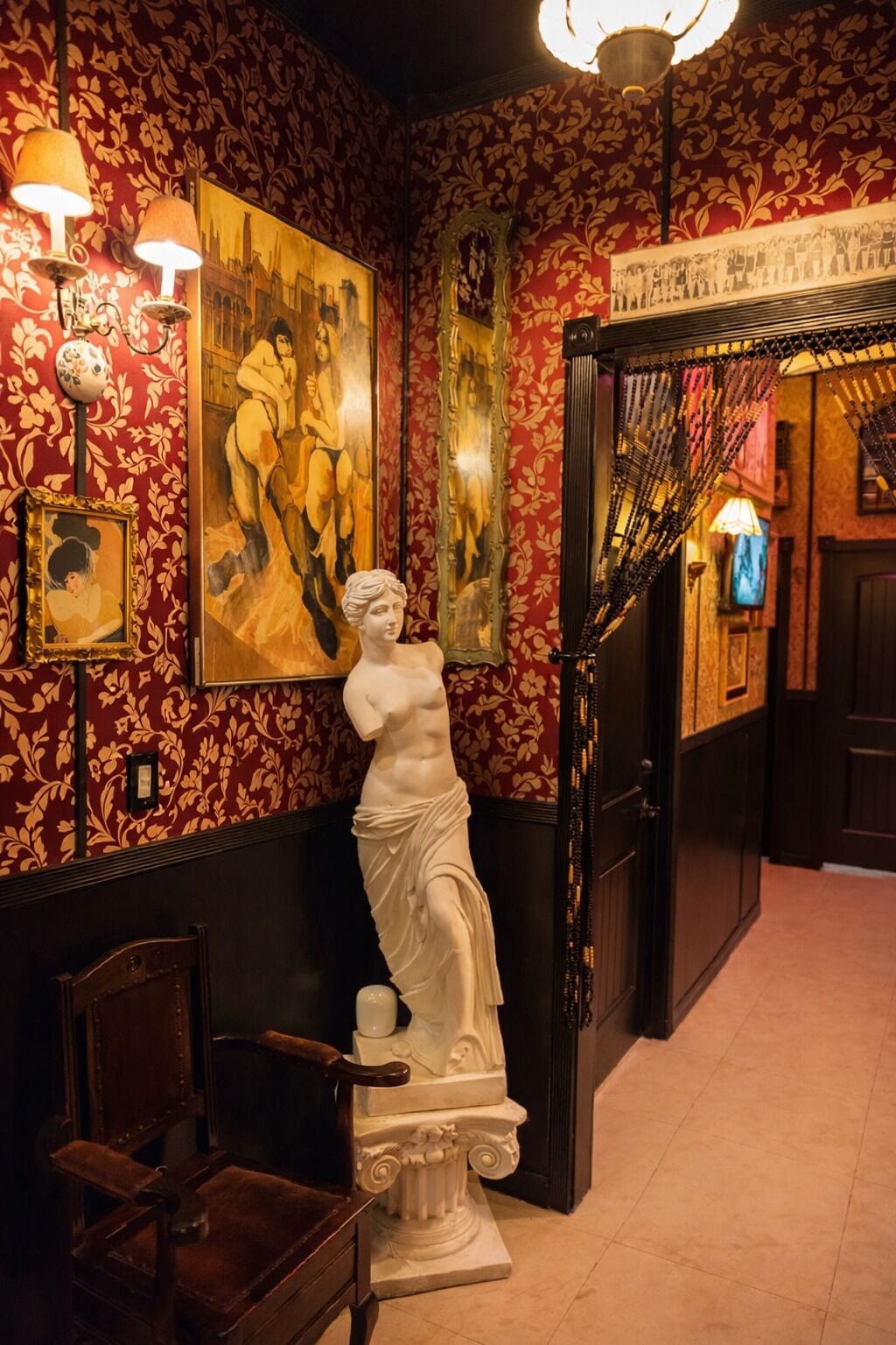 Un corridoio con carta da parati a motivi rossi, uno scultura di busto bianco e un quadro incorniciato.