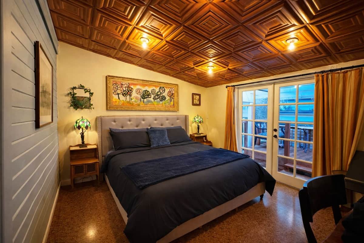 Une chambre avec un grand lit, un plafond en bois, un tableau et une vue sur l’extérieur.