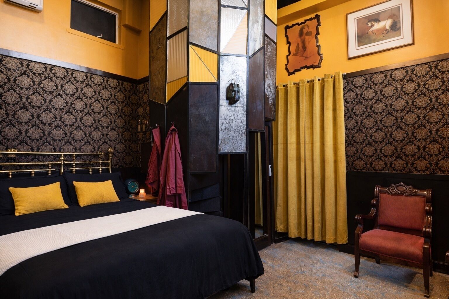 A bedroom with a large bed, a chair, and patterned wallpaper.