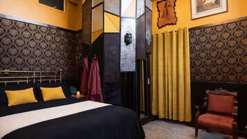 A bedroom with a large bed, a chair, and patterned wallpaper.