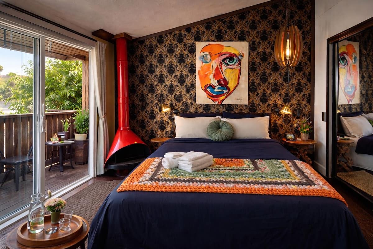 Une chambre avec un grand lit, une cheminée rouge et un balcon aménagé avec du mobilier d’extérieur.