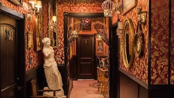 A hallway with ornate wallpaper, a chandelier, and classical statues.