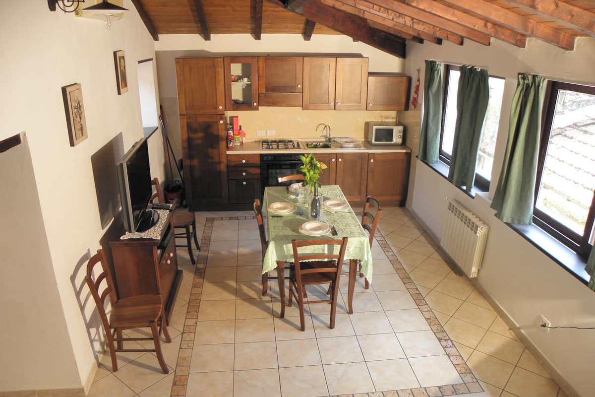 A kitchen with wooden cabinets, a dining table with chairs, a television, and a window with curtains.