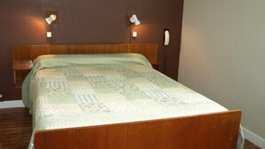 Une chambre à coucher avec une tête de lit en bois, un lit recouvert d’une couvre-lit à motifs et deux lampes fixées au mur.
