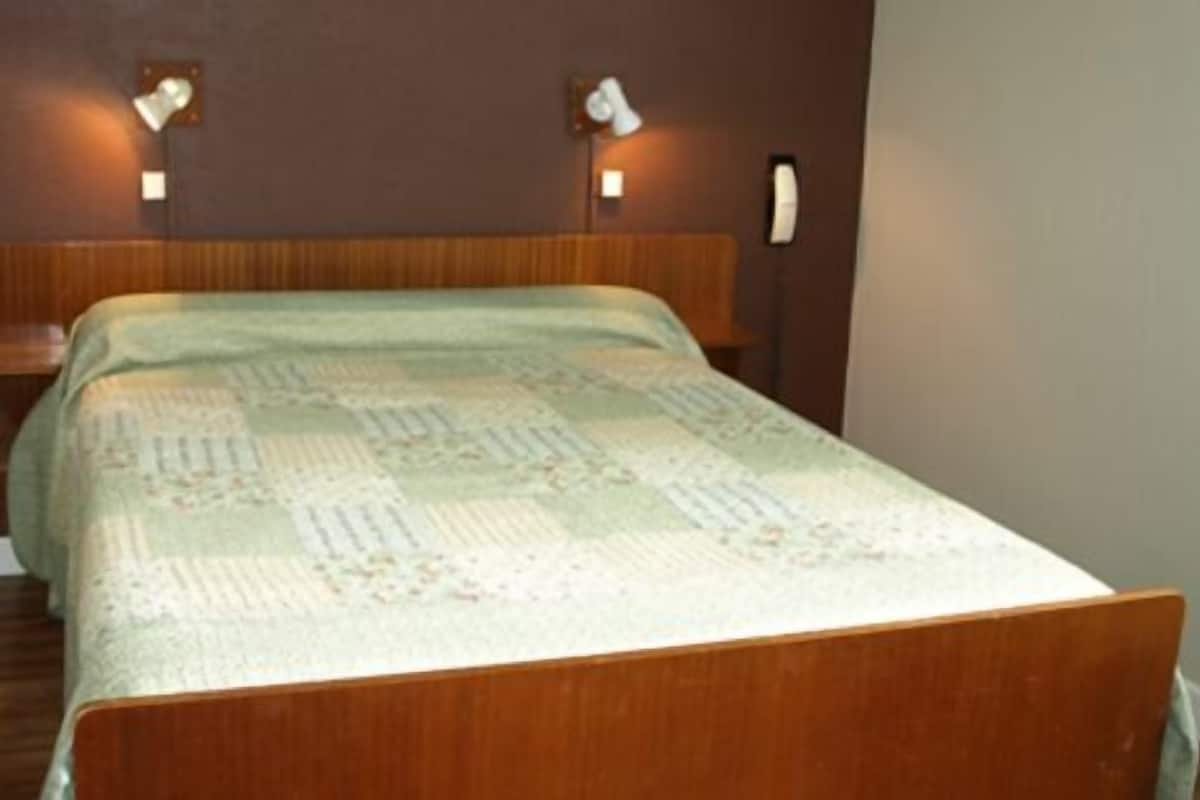 Ein Schlafzimmer mit einem hölzernen Kopfteil, einem Bett mit einem gemusterten Bettdecken und zwei Wandleuchten.