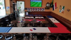 Un restaurant avec plusieurs tables et chaises, un téléviseur fixé au mur et un drapeau accroché au mur.