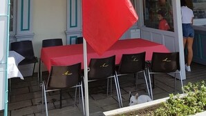 Un mât sur lequel flotte le drapeau français, des tables et des chaises disposées à l’extérieur pour créer un espace de détente, et un bâtiment doté d’un balcon.