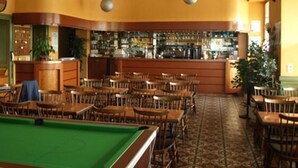 Une salle de billard équipée de plusieurs tables et de chaises, d’une table de billard et d’un bar avec des étagères remplies de bouteilles.