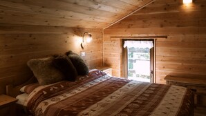 Une chambre confortable, aménagée dans un chalet en bois, avec un lit, une table de chevet, une lampe fixée au mur et une fenêtre donnant sur un paysage agréable.