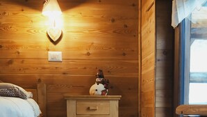 Une chambre confortable de style cabane, avec un intérieur en bois, un lit agrémenté d’un coussin à motifs, une table de chevet ornée d’un objet décoratif et un tapis blanc moelleux sur le sol.