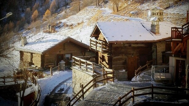 Un chalet de montagne rustique, avec une façade en bois, un escalier en pierre et un toit recouvert de neige.