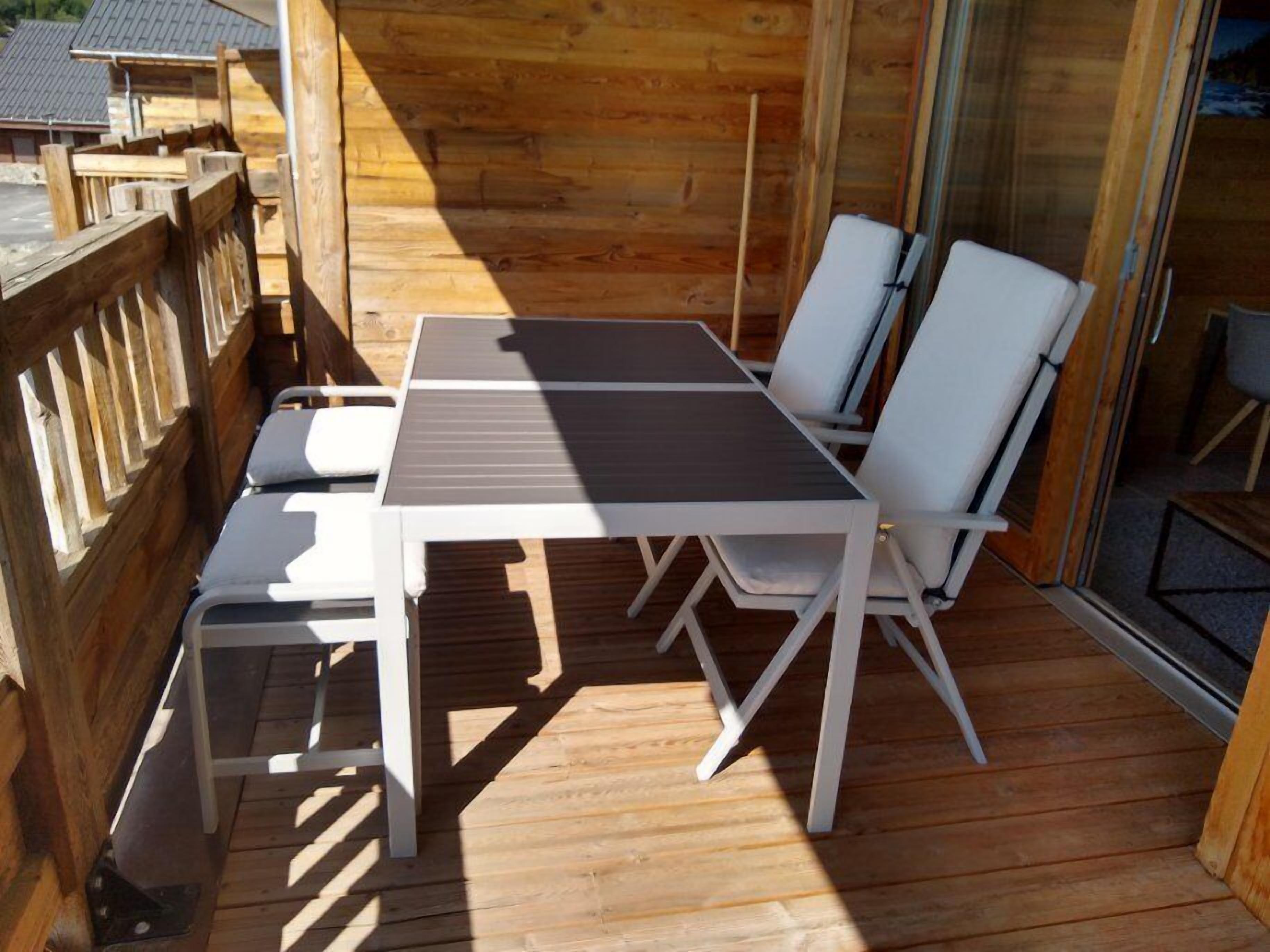 A wooden deck with a table and chairs, a wooden fence, and a glass door leading to a covered area.