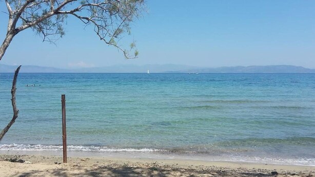 A beach with clear water, a sandy shore, and a distant sailboat. - Καλώς ήρθατε στην εξοχική κατοικία στην Αίγινα (Aegina)