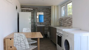 A compact kitchen with a washing machine, a sink, and a dining area with a table and chairs. - Καλώς ήρθατε στην εξοχική κατοικία στην Αίγινα (Aegina)