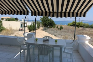 An outdoor patio with a striped awning, white plastic chairs, and a table with a bowl and apples.