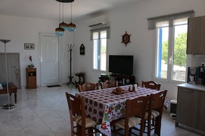A dining area with a table set for six, a television, and a kitchen area with cabinets and a coffee machine.