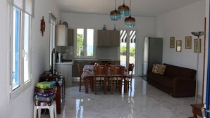 A spacious living area with a dining table, a sofa, and a kitchen in the background. - Καλώς ήρθατε στην εξοχική κατοικία στην Αίγινα (Aegina)