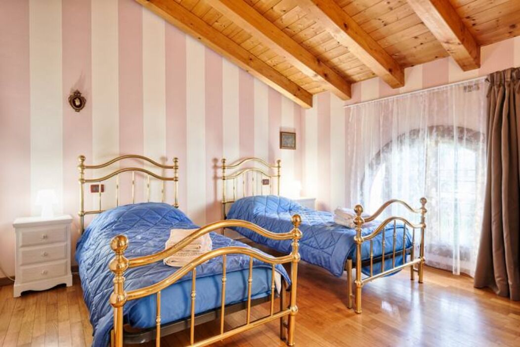 A room with two beds, wooden flooring, and a sloped ceiling.