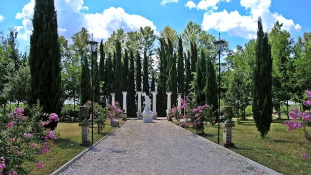 A gravel pathway leading to a white structure with columns, surrounded by tall trees and pink flowers. - Villa Navagero Erizzo - Ca' Rocchetto 2 (San Biagio di Callalta)