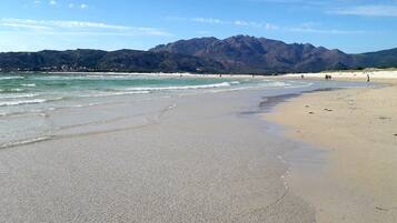 A beach with a mountain backdrop, sandy shore, and a few people walking.
