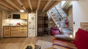 A cozy kitchen with wooden cabinets, a microwave, and a dandelion-themed door. A staircase leads to a stone-walled area with a fire extinguisher.