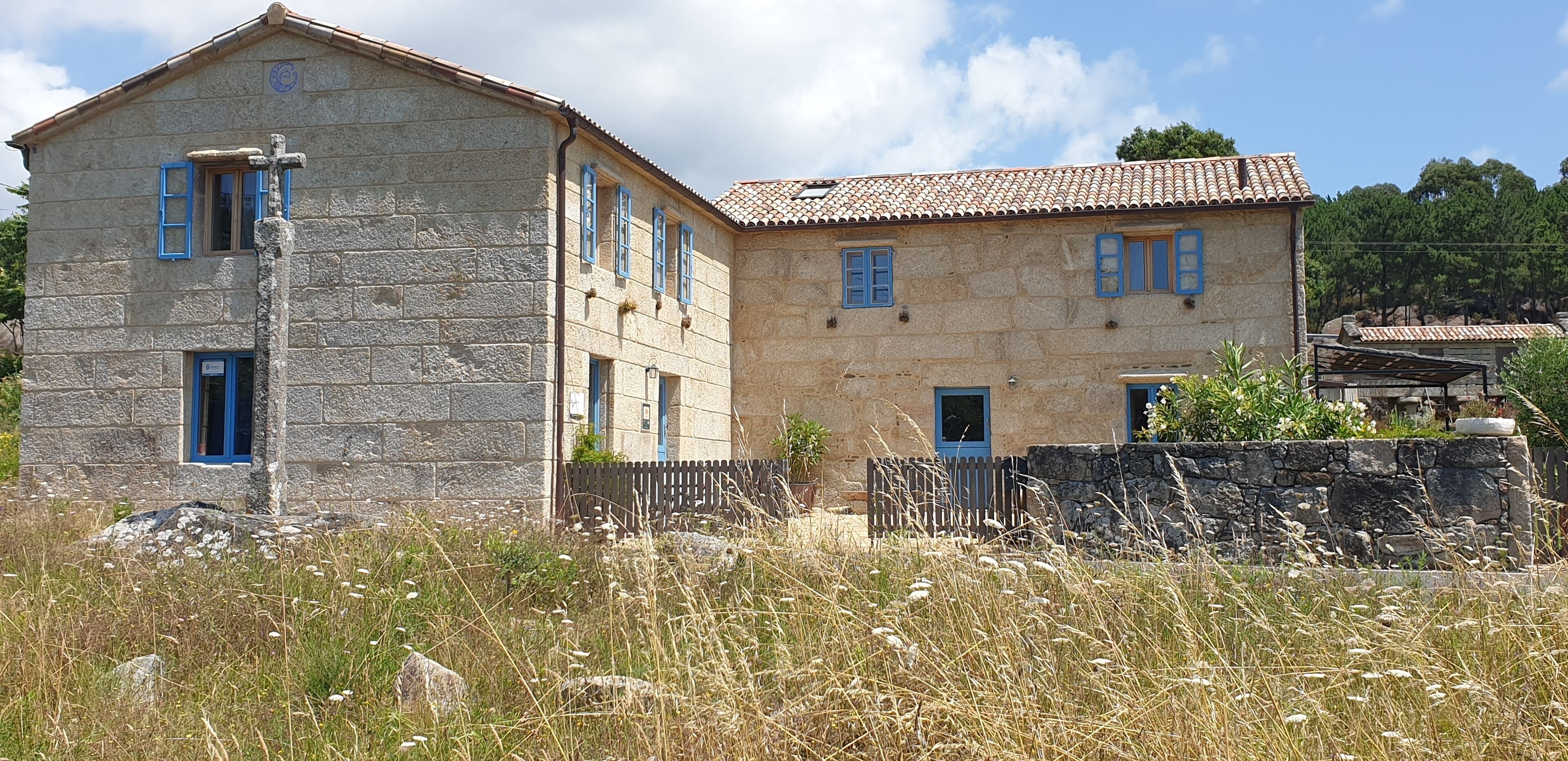 A stone building with a tiled roof, a wooden fence, and a stone wall in front.
