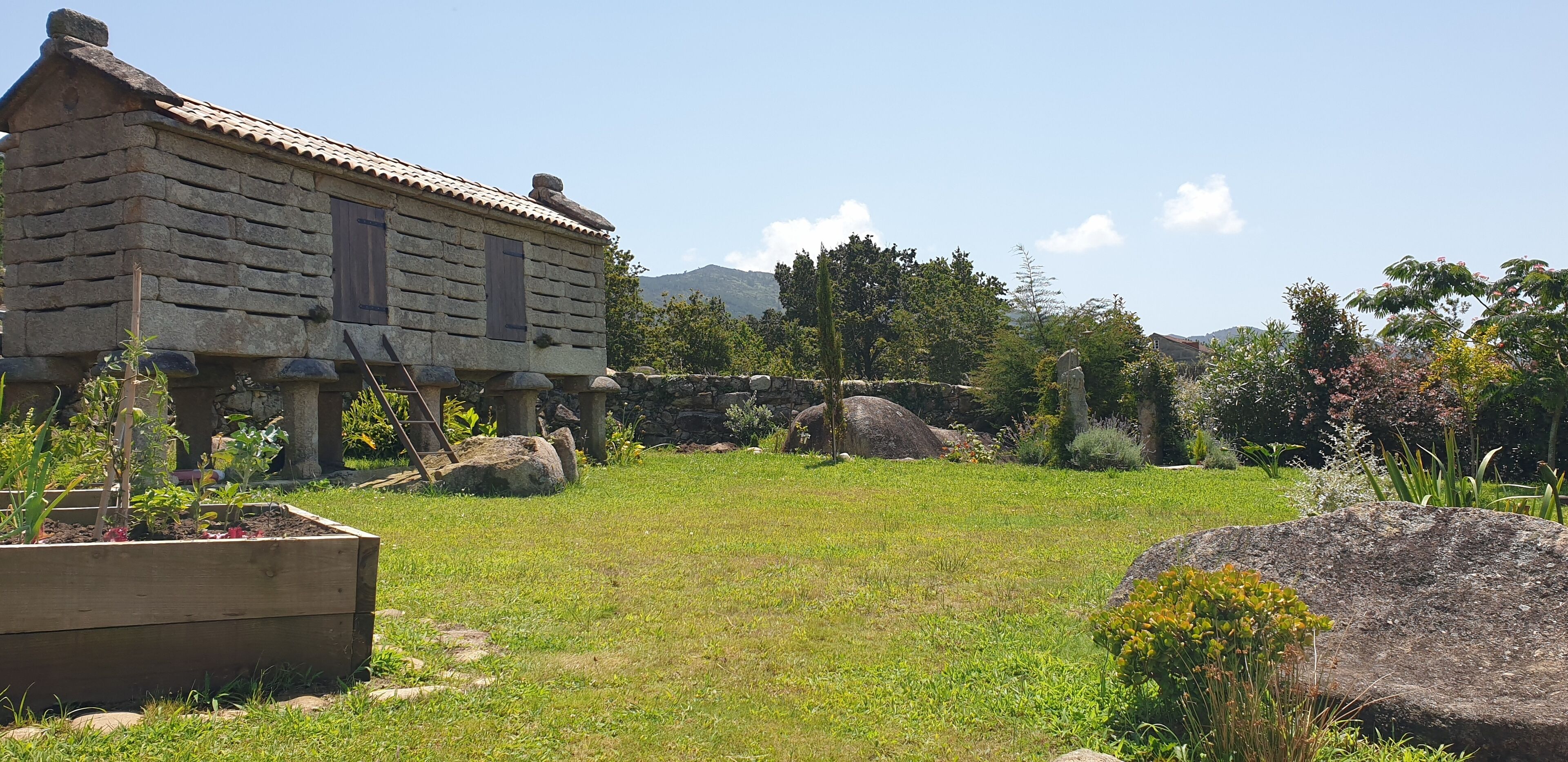 A rustic stone house with a wooden deck and a garden with rocks and plants.