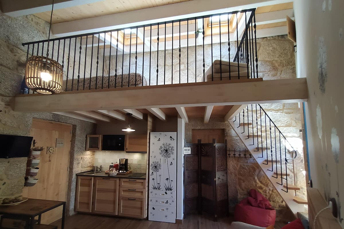 A spacious living area with a kitchen, a dining table, a sofa, and a staircase leading to an upper level.