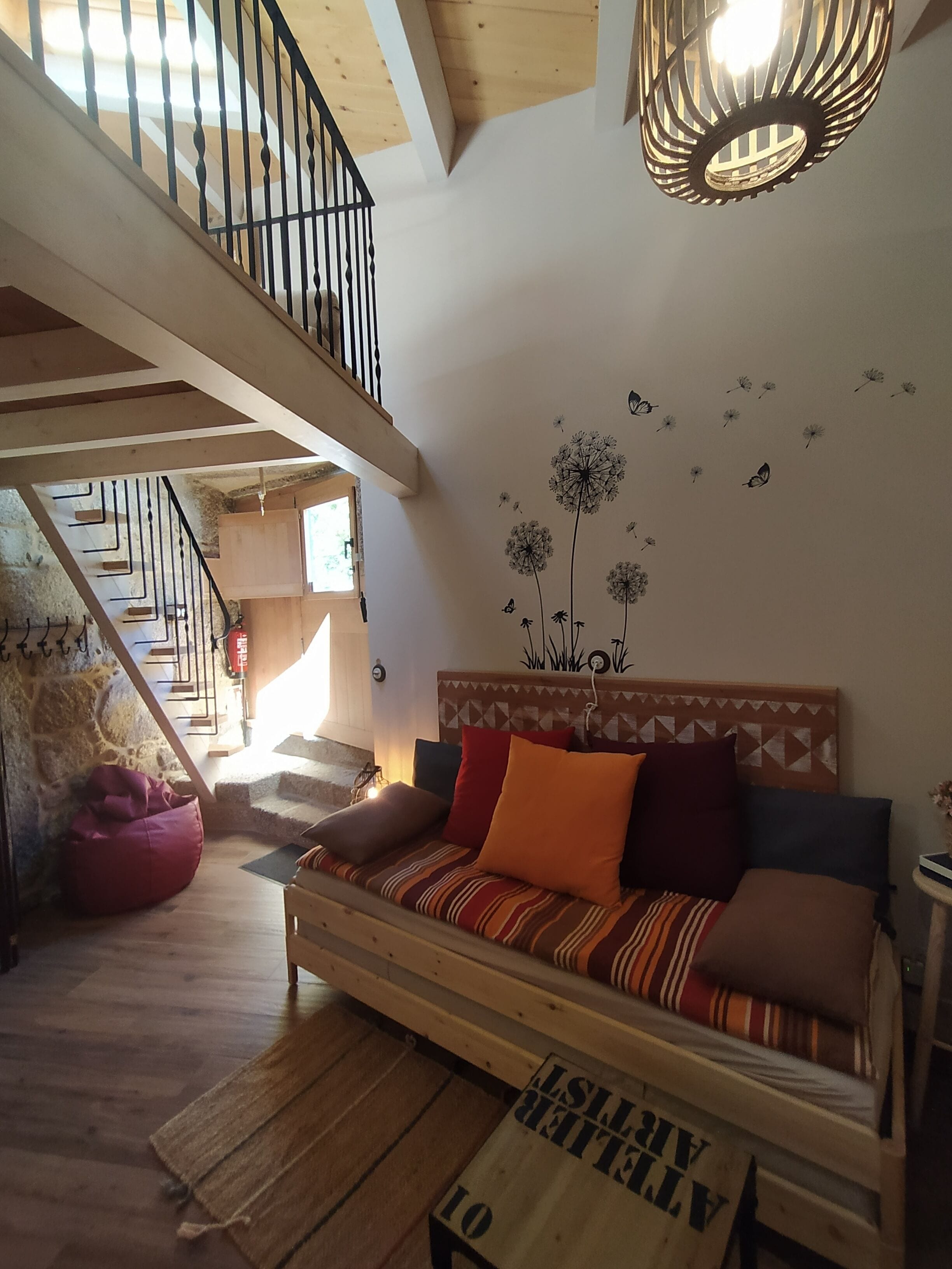 A cozy living room with a wooden sofa, a red bean bag, and a wall decal of dandelions and butterflies.