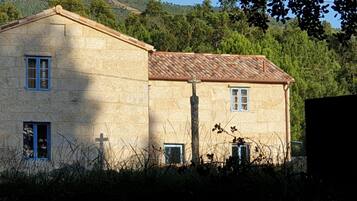 A stone building with a tiled roof, two windows, and a cross on the wall.