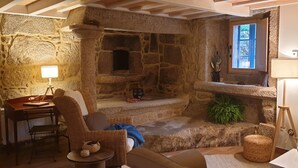 Une pièce chaleureuse avec une cheminée en pierre, un bureau avec une lampe, des meubles en osier et une petite table sur laquelle se trouve un bol.