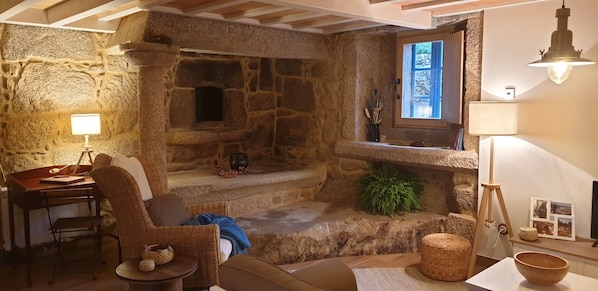 Una habitación acogedora con chimenea de piedra, un escritorio con lámpara, muebles de mimbre y una pequeña mesa con un cuenco.