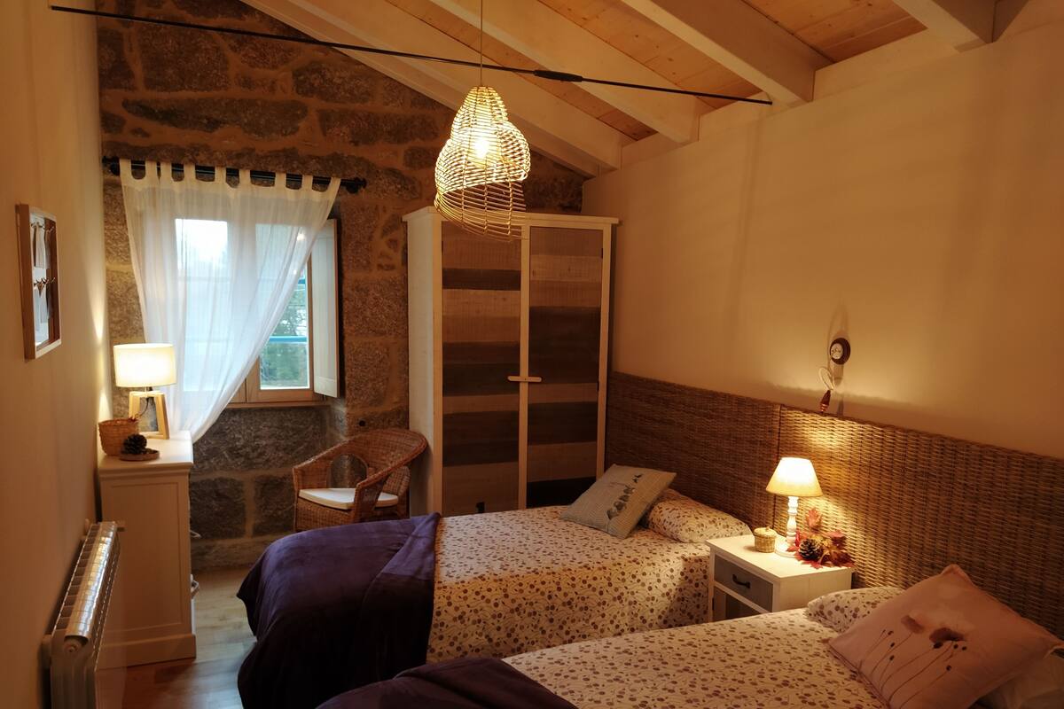 A bedroom with two beds, a wardrobe, a chair, and a window with curtains.