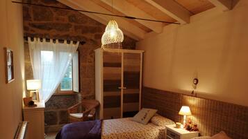 A bedroom with two beds, a wardrobe, a chair, and a window with curtains.