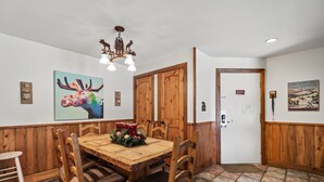 A dining area with a wooden table and chairs, a chandelier, and wall art. - Family-Friendly Comfort at Timber Run – 2-Bedroom Condo Near the Slopes! (Steamboat Springs)