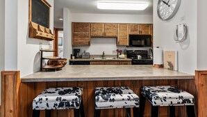 A kitchen with wooden cabinets, a microwave, a coffee maker, and a clock on the wall. - Family-Friendly Comfort at Timber Run – 2-Bedroom Condo Near the Slopes! (Steamboat Springs)