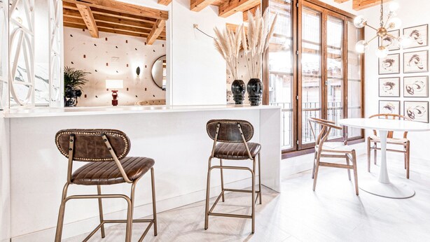 A modern kitchen with two bar stools, a dining table, and a large window with decorative pampas grass. - ~TIVOLI~ by myhomeintoledo.com (Toledo)