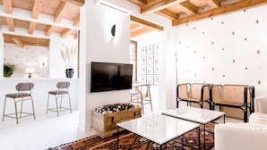 A modern living room with a flat-screen TV, wooden ceiling beams, a patterned rug, and a mix of modern and rustic furniture. - ~TIVOLI~ by myhomeintoledo.com (Toledo)