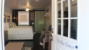 Un dormitorio con cama, una silla, un escritorio, un ventanal y una puerta con la leyenda 'The Blue Flower'.